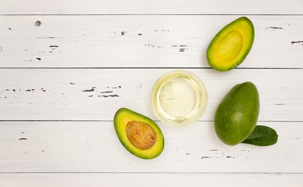 Aceite de aguacate en una taza de vidrio y fruta de aguacate sobre un fondo de madera blanca, vista superior, copyspace