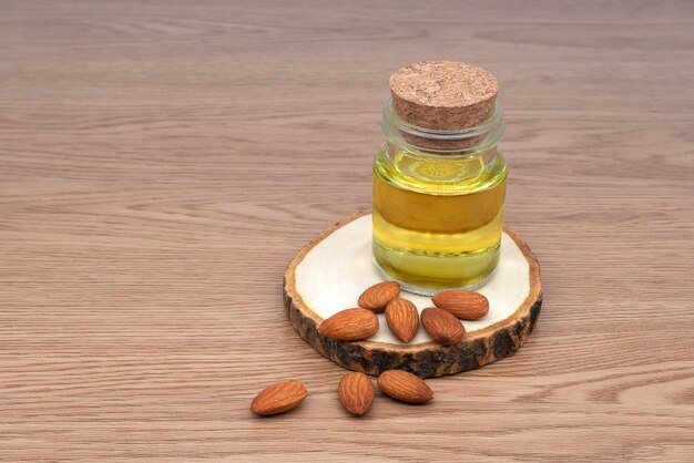 Aceite de almendras en botella de vidrio y grupo de nueces de almendras sobre fondo de textura de madera Aceite de almendras con semillas de almendras