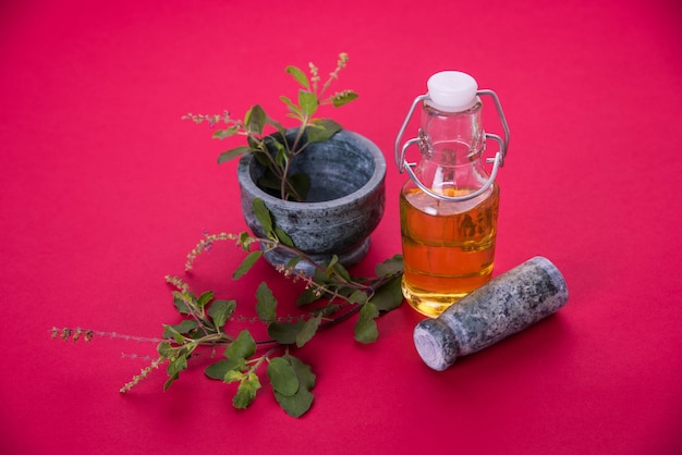 Aceite ayurvédico de Tulsi, extracto de hierba reina en botella de vidrio con ramas de albahaca santa verde fresca y mortero con mortero. Aislado sobre fondo de colores. enfoque selectivo