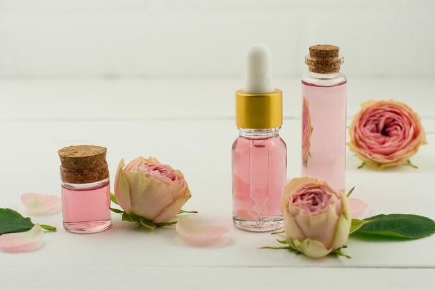 Aceite de belleza facial hecho de flores color de rosa sobre fondo blanco de madera con flores frescas. Tratamiento facial y corporal para el cuidado de la piel. Aromaterapia.