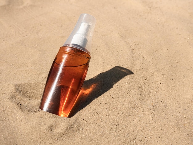 Aceite de bronceado en una botella transparente rociada sobre la arena bajo el sol brillante Protector solar cosmético para el cuidado de la piel