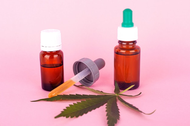 Aceite de cáñamo para uso médico, botellas con extracto de cannabis medicinal en primer plano de fondo rosa.