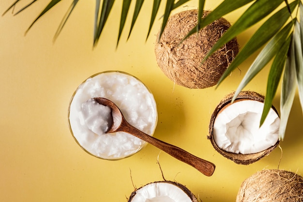 Aceite de coco y cocos en una con hojas tropicales.