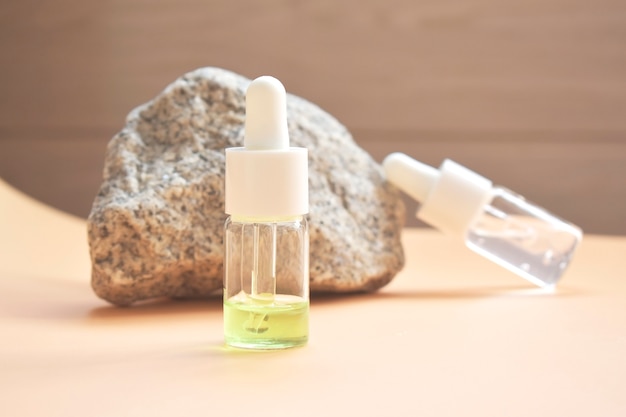 Aceite cosmético en botella con pipeta para rostro y cuerpo sobre un fondo natural con una decoración en forma de piedra natural. Espacio para texto.