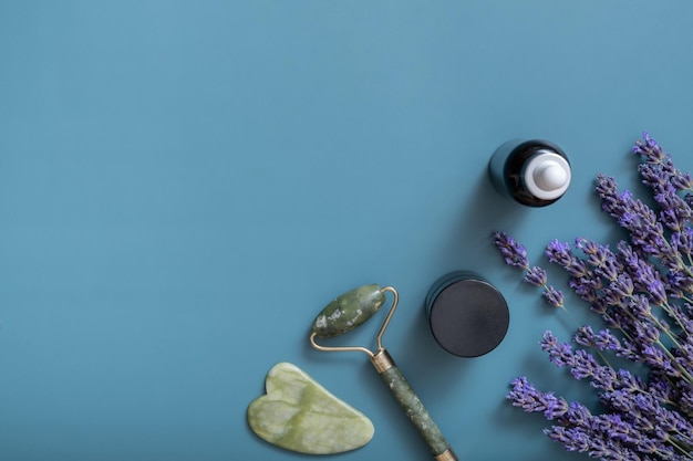 Aceite cosmético o suero en botella de pipeta y masajeador facial con flores de lavanda en la vista superior de fondo de color