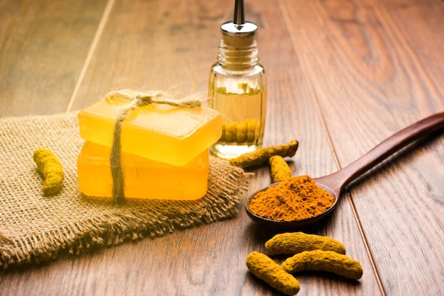 Aceite esencial de cúrcuma con jabón y palos de Haldi secos y polvo en una cuchara de madera