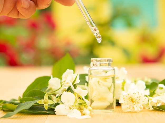 Aceite esencial de jazmín en una botella de vidrio sobre un fondo de flores de jazmín sobre una mesa de madera