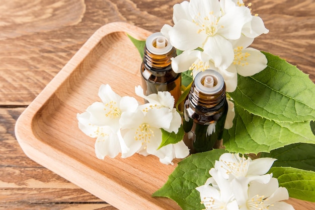 Aceite esencial de jazmín natural en dos botellas médicas de vidrio con un cuentagotas en una bandeja de madera entre las flores de jazmín el concepto de spa
