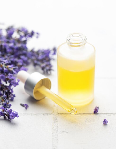 Aceite esencial natural de lavanda y lavanda fresca sobre un fondo de azulejos blancos