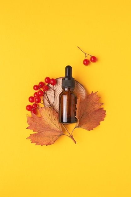 Aceite esencial natural de viburnum en botella con un cuentagotas sobre fondo amarillo con una rama de viburnum maduro de otoño