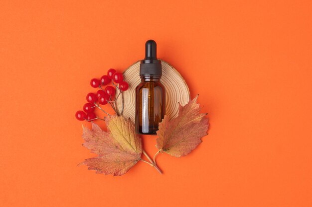 Aceite esencial natural de viburnum en botella con cuentagotas sobre fondo naranja con una rama de viburnum maduro de otoño