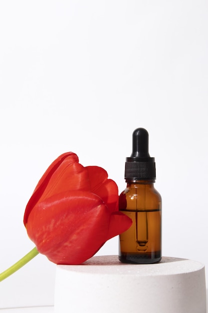 Aceite facial de colágeno de belleza en un frasco cuentagotas de vidrio con tulipán en el podio Sesión de moda de envases cosméticos Aceite esencial con ingredientes naturales