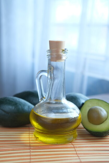 Aceite en frasco de vidrio y una rodaja de aguacate en la mesa de madera