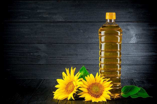 Foto aceite de girasol con flores sobre fondo rústico negro