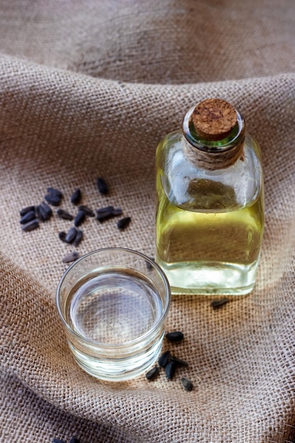 Aceite de girasol en un vaso de botella con semillas sobre fondo de tela de lona de arpillera