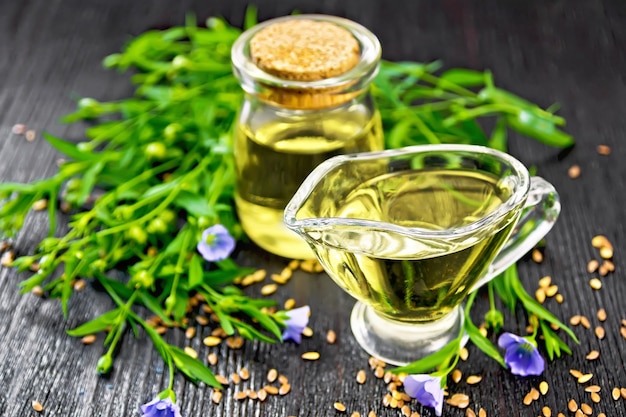 Aceite de linaza en un frasco de vidrio y salsera con semillas, hojas y flores de lino sobre un fondo de tabla de madera