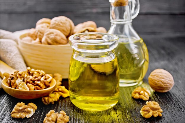 Aceite de nuez en tarro y decantador, nueces en caja, cuchara y en la mesa sobre fondo de tablero de madera