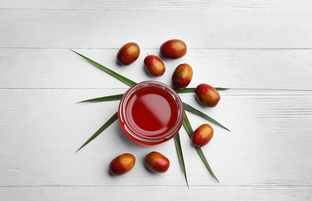 Aceite de palma en frasco de vidrio con hojas tropicales y frutas en una mesa de madera blanca plana