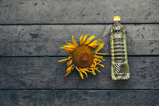 Aceite prensado en frío y un hermoso y grande girasol en flor sobre un fondo de madera. Pétalos de girasol amarillo. Un fondo natural asociado al verano.