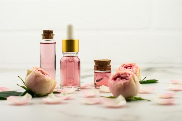 Aceite de rosa y agua de rosas en botellas de vidrio con el telón de fondo de una pared de ladrillo blanco, capullos y pétalos de rosa. producto de cuidado facial anti-envejecimiento.