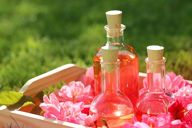 aceite de rosa. Spa con rosa. aceite de pétalos de rosa. aceite de rosa natural en botellas de vidrio y rosas rosadas en una bandeja de madera. Concepto de masaje, aromaterapia y cosmética orgánica.