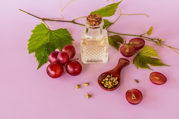 Aceite de semilla de uva en una botella transparente de vidrio con un tapón sobre un fondo rosa y un alto contenido de vitaminas minerales de vid