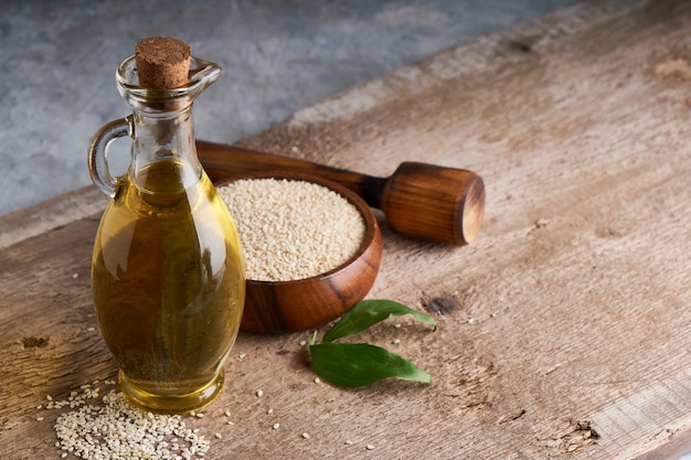 Aceite de sésamo en frasco de vidrio y semillas de sésamo en mesa de madera Copia espacio Rústico