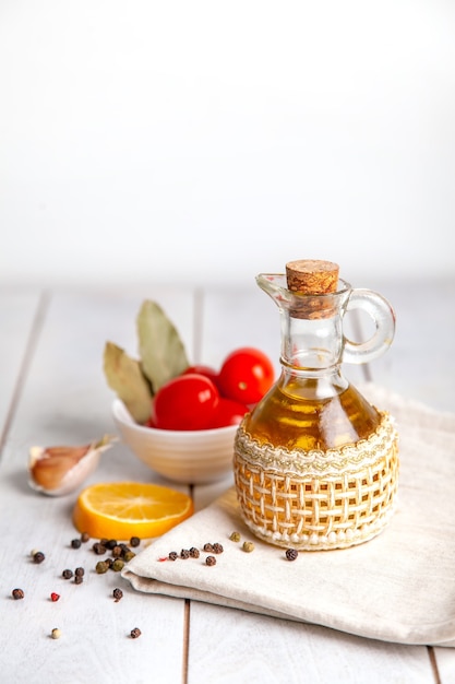 Aceite vegetal en una botella sobre una toalla con tomate, limón, pimienta y laurel con espacio de copia.