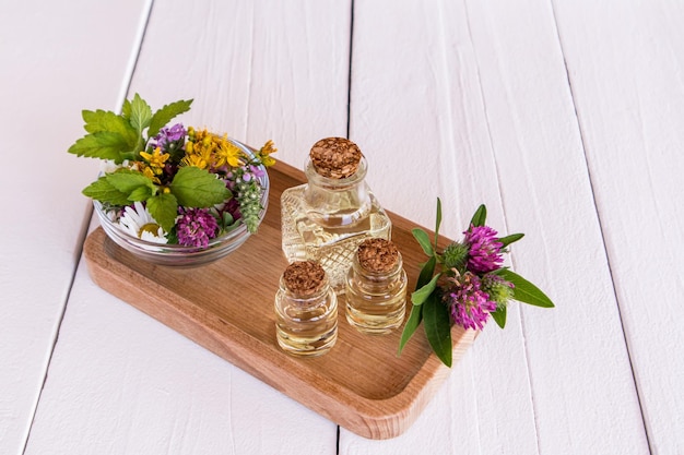 Aceites naturales orgánicos de flores de pradera en botellas de vidrio sobre una bandeja de madera de fondo blanco con flores de pradera en un tazón enfoque selectivo