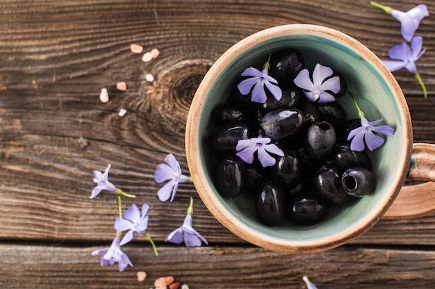 Aceitunas negras en un cuenco de cerámica sobre un fondo de madera decorado con flores azules