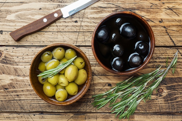 Aceitunas negras y verdes en cuencos de madera en mesa de madera