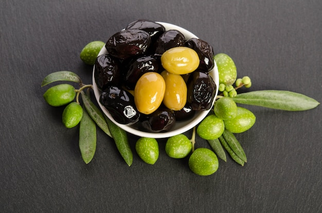 Aceitunas negras y verdes en un recipiente aislado sobre un fondo gris