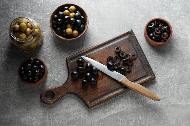 Foto aceitunas en tazones y tablero de cocina de tarro y cuchillo en la vista superior de fondo gris