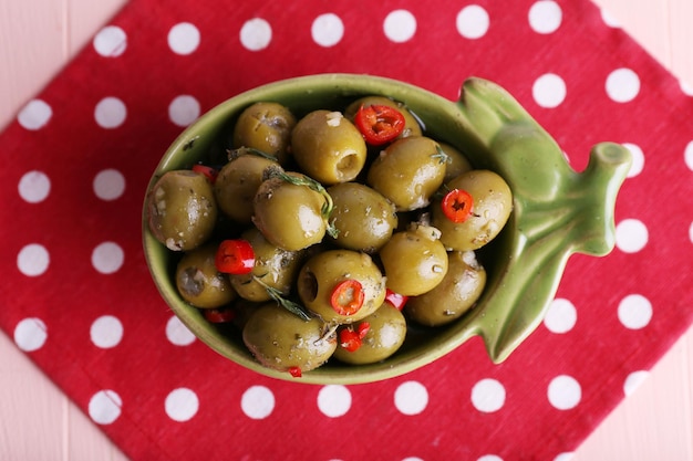 Aceitunas verdes en aceite con especias y romero en un recipiente sobre mesa de madera