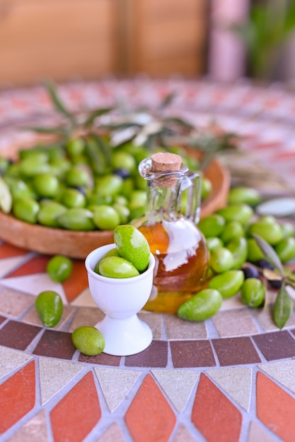 Aceitunas verdes frescas con ramas y hojas. Cosecha estacional en Italia. Botella de aceite de oliva y bayas en una mesa de piedra.