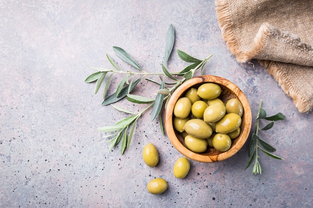 Aceitunas verdes frescas en un recipiente y rama de olivo en piedra rústica