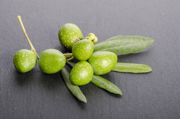 Aceitunas verdes jóvenes con hojas sobre fondo negro