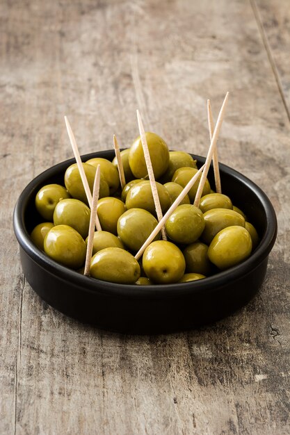 Aceitunas verdes en un recipiente en la mesa de madera