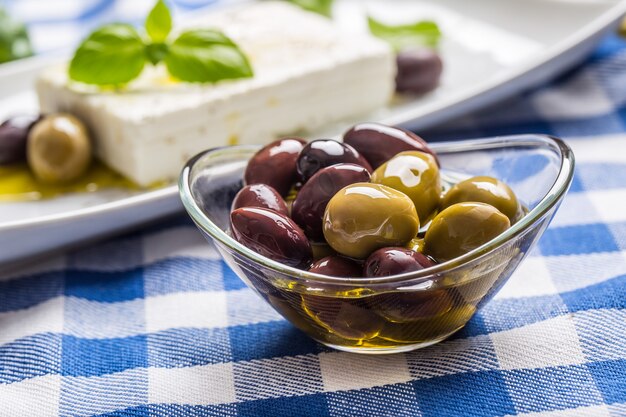 Aceitunas verdes y rojas en un tazón con aceite de oliva y queso feta griego de fondo.