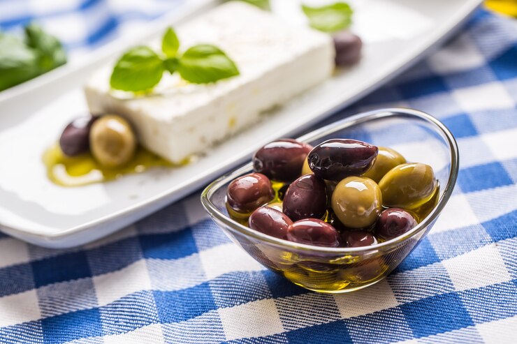Aceitunas verdes y rojas en un tazón con aceite de oliva y queso feta griego de fondo.