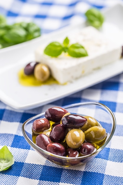 Aceitunas verdes y rojas en un tazón con aceite de oliva y queso feta griego de fondo.