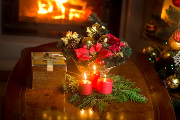 Acendendo velas perto da árvore de Natal decorada, caixa de presente e grinalda tradicional