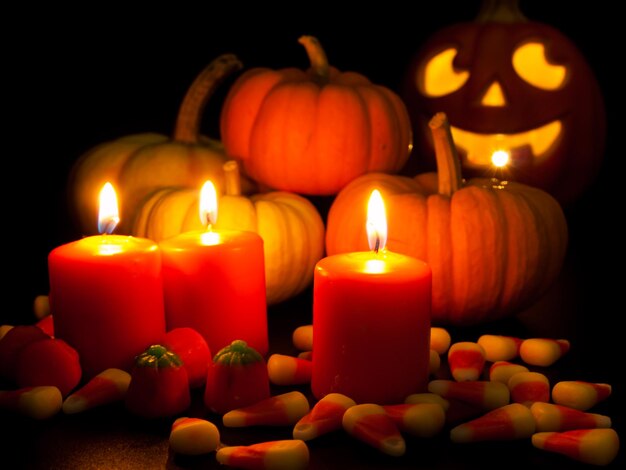 Acendeu velas laranja com pequenas abóboras e jack-o'-lantern em fundo preto.