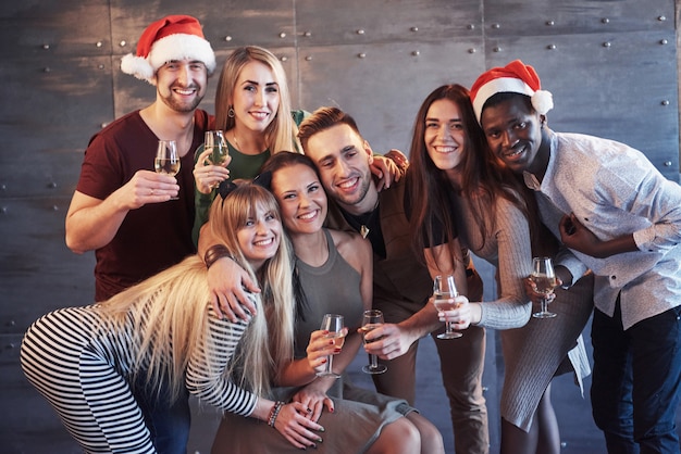 ¡Se acerca el año nuevo! Grupo de alegres jóvenes multiétnicos con sombreros de Santa en la fiesta, posando el concepto de gente de estilo de vida emocional