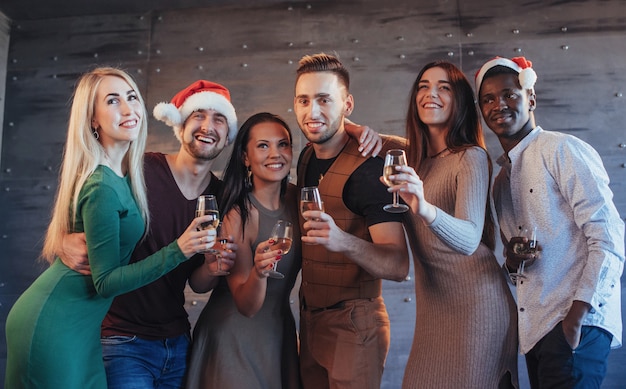 ¡Se acerca el año nuevo! Grupo de alegres jóvenes multiétnicos con sombreros de Santa en la fiesta, posando el concepto de gente de estilo de vida emocional