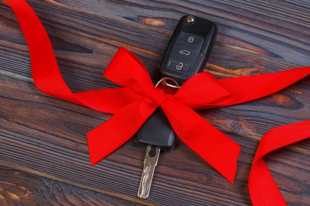 Acercamiento de las llaves del auto con lazo rojo como presente en el fondo de madera