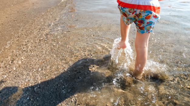 Acercamiento de los pies del niño corriendo en agua de mar en la playa.