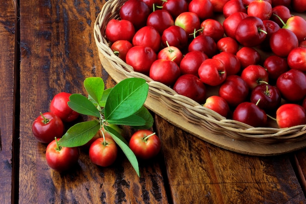 Acerola-Kirsche roh, frisch, im Korb mit Herzform auf rustikalem Holztisch