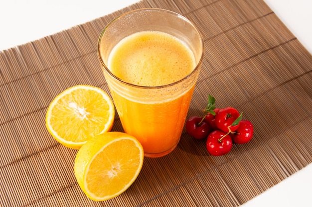 Acerola orgânica fresca e suco de laranja em um copo de vidro com frutas laranja fatiadas e bagas de acerola em um jogo americano de bambu em fundo branco em vista superior