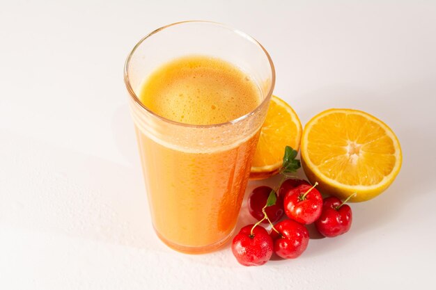 Acerola orgánica fresca y jugo de naranja en un vaso con media naranja y bayas de acerola en una foto de estudio blanca y limpia en la vista superior